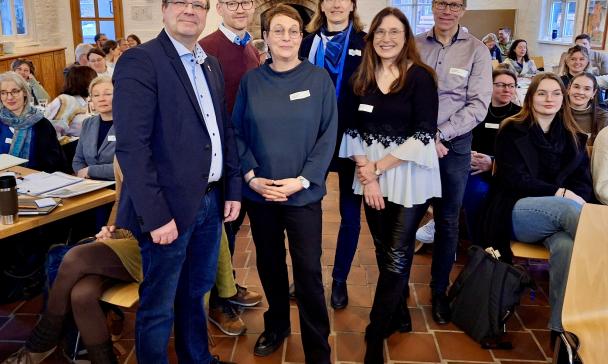 Sechs Personen in einem Vortragsraum zwischen Stuhlreihen
